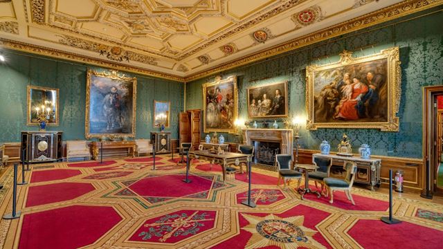A large turquoise drawing room with gold and red carpet and painting lined walls at windsor castle.