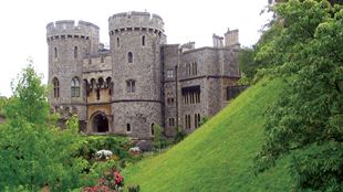 The exterior of Windsor Castle with greenery and a green mount on the right side