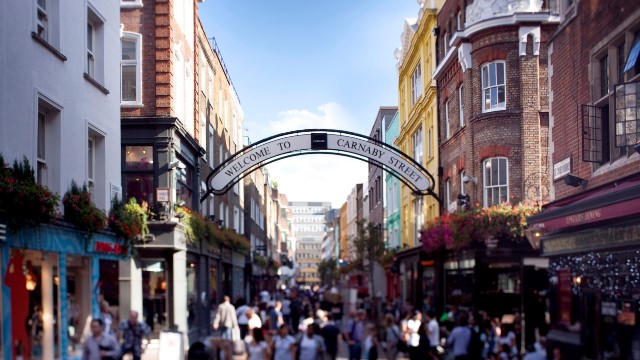 Treat yourself at Carnaby Street's many shops. Image courtesy of Carnaby Street. People walking thorugh Carnaby Street, with blue skies above.
