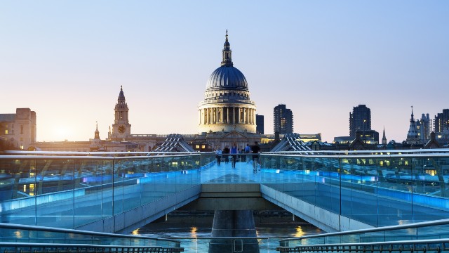 Millennium Bridge lit up in the early evening, with St Paul's Cathedral in the background.