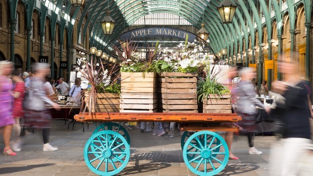 A cart topped with green plants in the middle of Covent Garden's Apple Market.