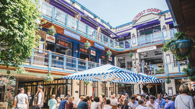 People sitting under umbrellas enjoying their time eating and drinking at Kingly Court.