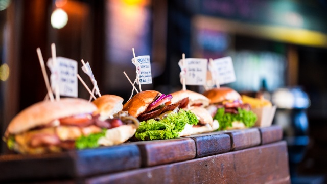 Burgers lined up on a wooden counter.
