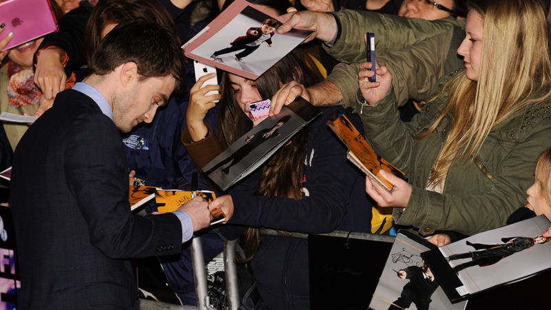 Daniel Radcliffe signs a fans photograph at BFI Southbank as other fans take photos and smile at him