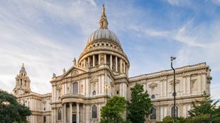 Sweeping view of the front of St Paul's Cathedral with a blue sky in the background.