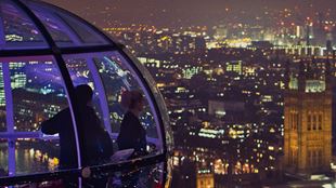 Two visitors look out onto Big Ben and London after dark from a glass capsule on the London Eye.