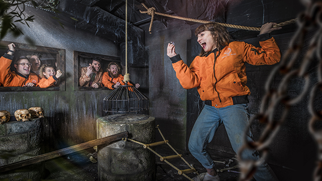 Crystal Maze LIVE Experience, Image courtesy of Buy a Gift. A woman wearing an orange jacketis cheered up by her team after finding a clue in a dungeon