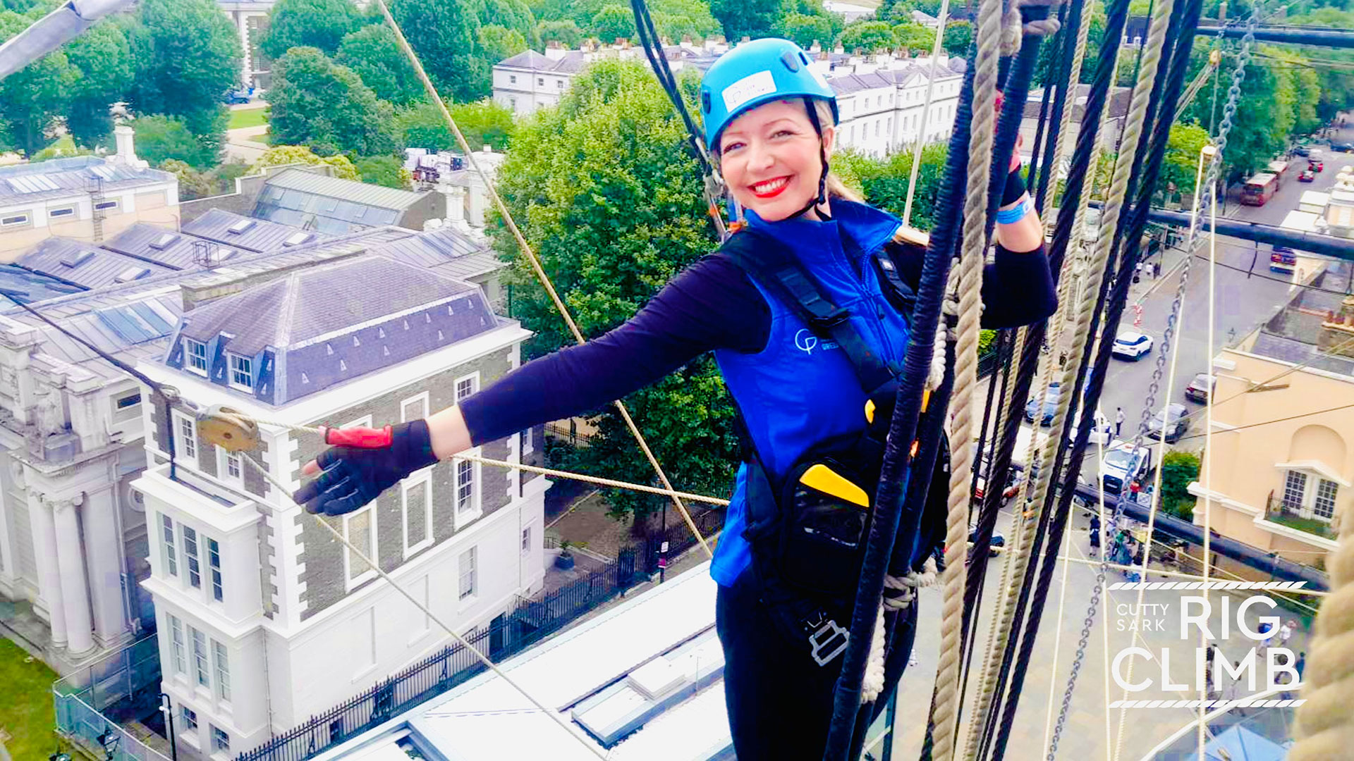 Admire the views from the iconic Cutty Sark. Image courtesy of Wire & Sky. A woman smiling while holding onto the Cutty Sark's ropes high up above the rooftops of Greenwich