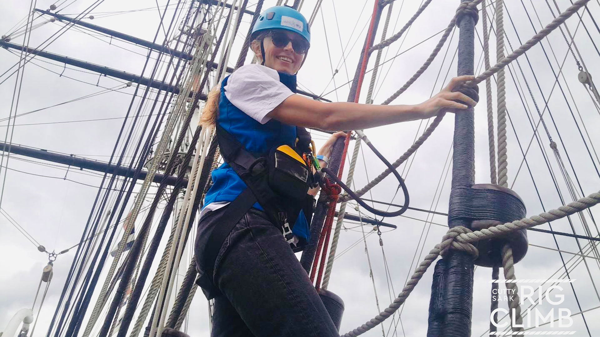Climb to great heights on the Cutty Sark Rig Climb Experience in Greenwich. Image courtesy of Wire & Sky. A woman wearing climbing equipment holding onto the ratlines of the Cutty Sark about to climb.