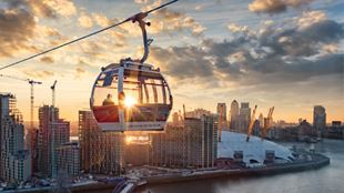 IFS Cloud Cable Car flying over London's O2 arena, high rises and the river Thames.