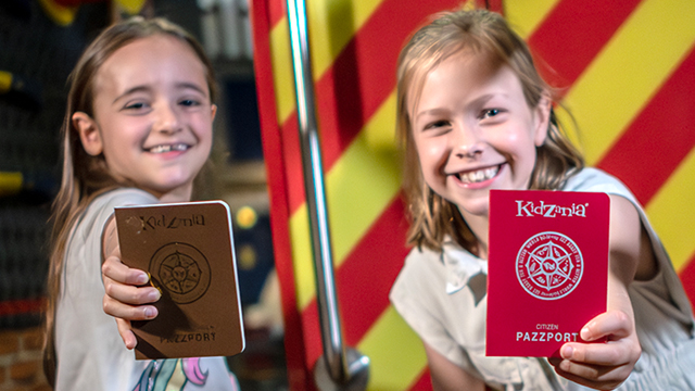 Bring the kids to KidZania, the only place in London where they can try different careers. © visitlondon.com/Michael Barrow Two kids smiling at the camera and proudly showing their KidZania passports.