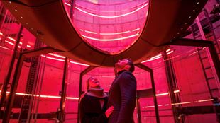 Two people stand shrouded in red light in the lift 109 at battersea power station.