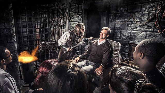 The Torturer at The London Dungeon. Image courtesy of The London Dungeon. A scared man sitting in a chair while another man in medieval costume tortures him