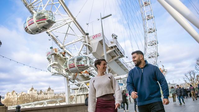 Two people walk in front of the pods of the London Eye. 