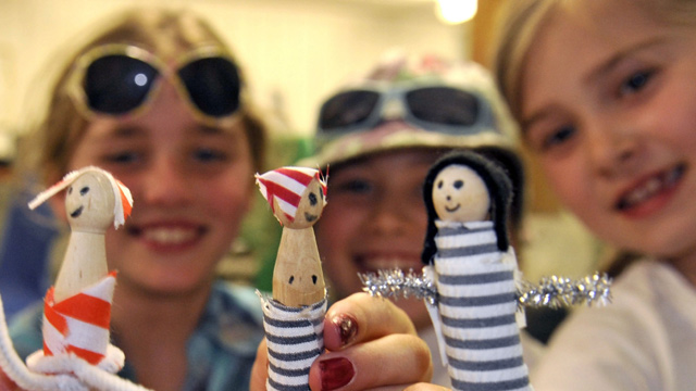 Three kids holding up sailor figures, smiling.