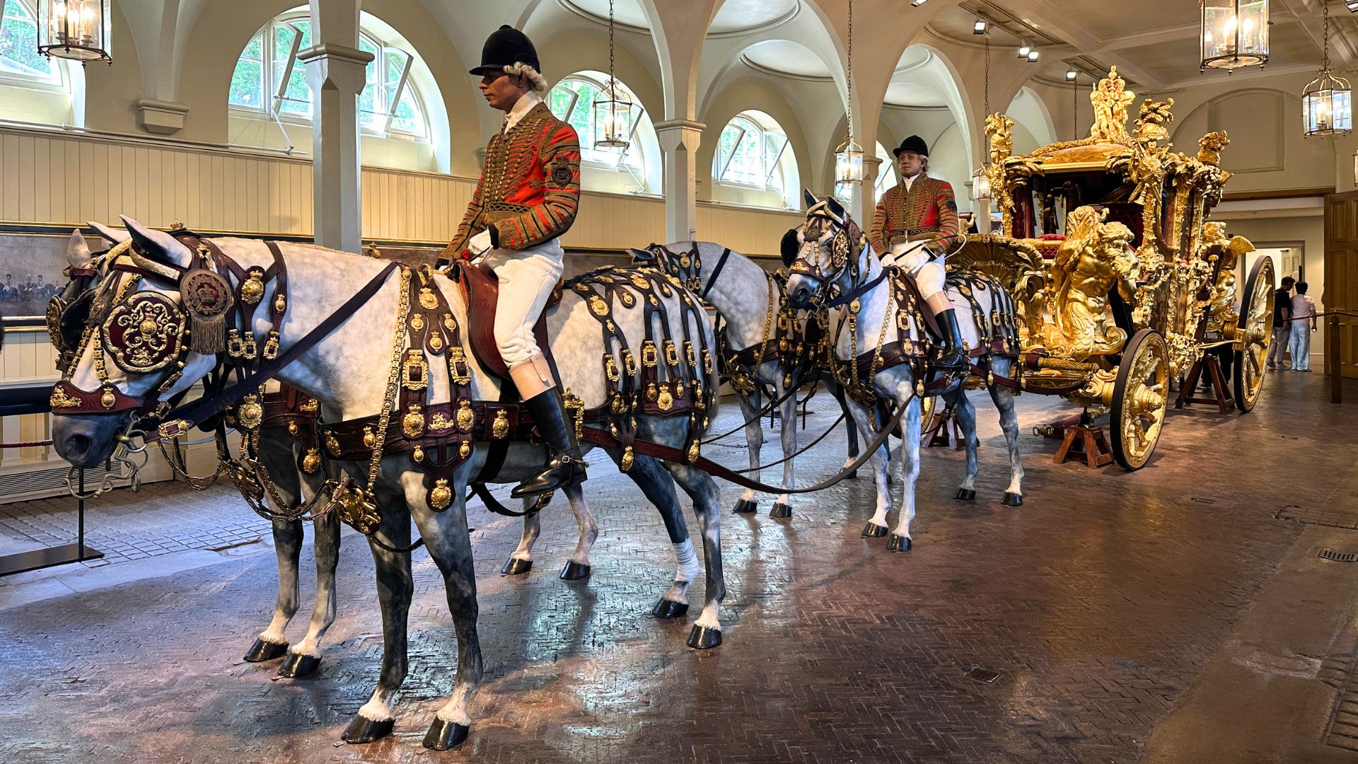 The spectacular Gold State Coach, over 260 years old, harnessed with model horses and riders in full ceremonial dress at the Royal Mews. Photo credit: Kirstine Spicer The Gold State Coach on display at the Royal Mews, with model horses and riders in ceremonial uniforms.