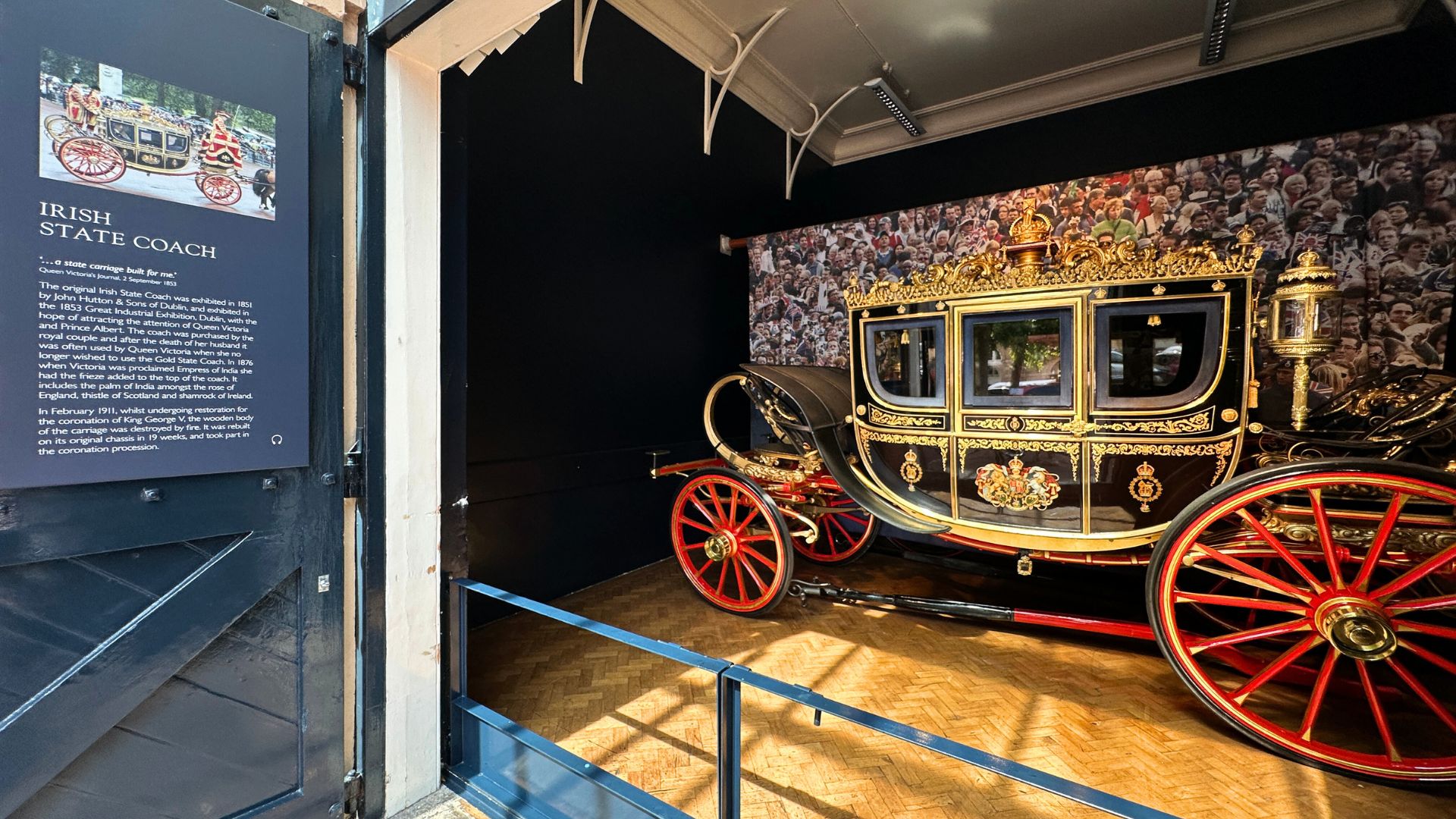 The historic Irish State Coach on display at the Royal Mews, Buckingham Palace – used by Queen Victoria and restored for King George V’s coronation. The Irish State Coach with gold detailing and red wheels, displayed with an information panel at the Royal Mews.