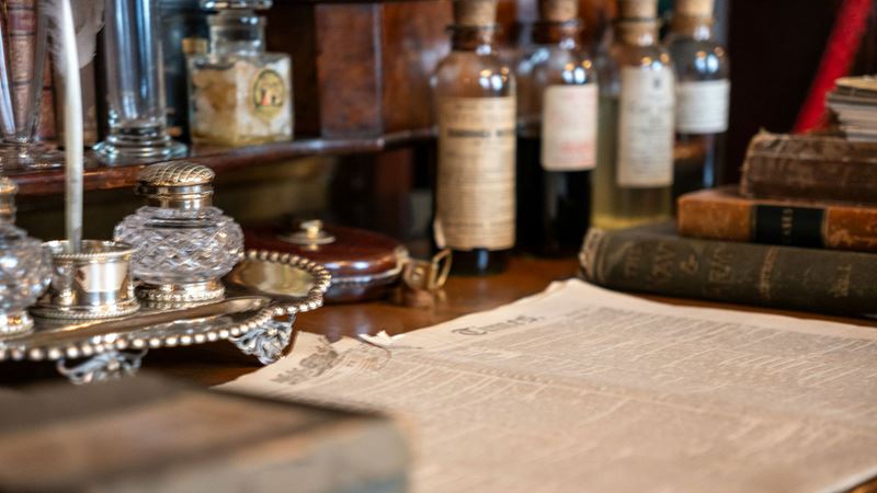 Browse through objects on display inside The Sherlock Holmes Museum at 221b Baker Street. Credit: Vitaliy Burov. Image courtesy of Unsplash. Old newspaper, glass bottles and books on display inside The Sherlock Holmes Museum in London.