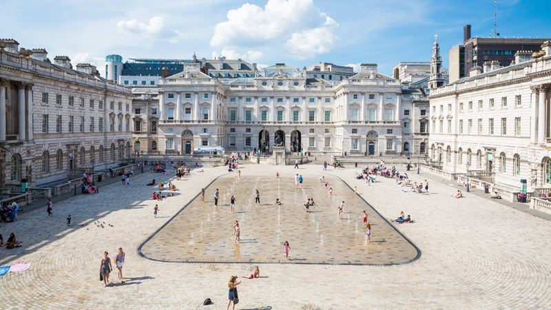 Courtyard view of Somerset House with fountain in the centre and people surrounding.
