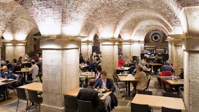 People sit at tables under the stone arches of the cafe in the crypt. 