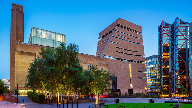 The back view of Tate Modern with glass buildings in the background on a clear evening in London.