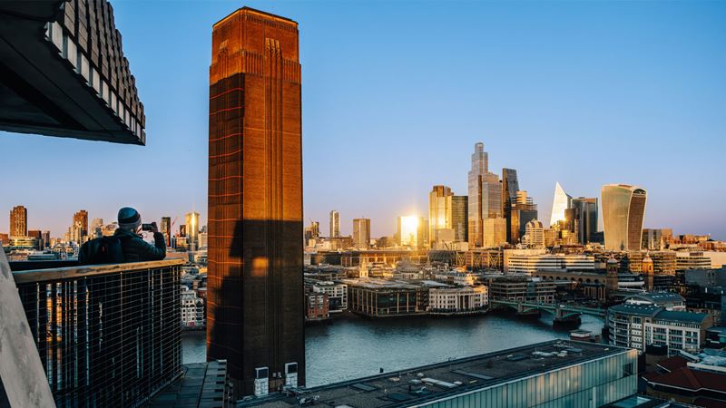 Spot incredible scenes from Tate Modern's viewing platform and restaurant. Credit: Michael Barrow. Image courtesy of London & Partners. Person standing on the Tate Modern viewing terrace taking a picture of the landmarks in the distance.