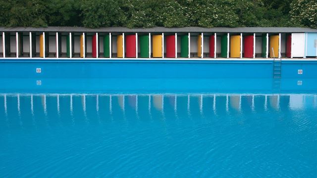 Looking across the pool at the colourful yellow, green and red doors of Tooting Bec Lido.