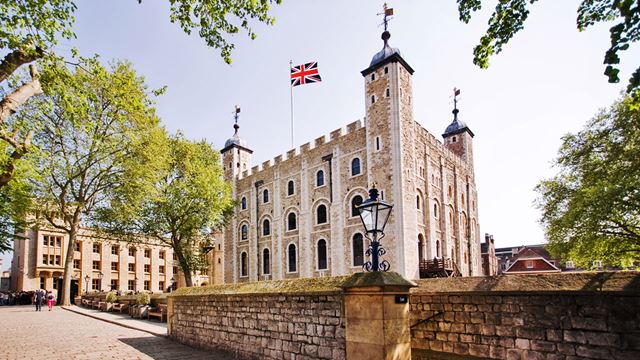 The White Tower, a tall white building standing in the middle of the Tower of London, has the Union Jack flying high.