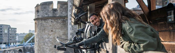 Two people lean over the ramparts at the Tower of London, one holding a crossbow.