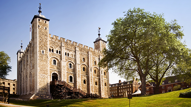 Tower of London © Shutterstock / Justin Black. The Tower of London, on a clear, bright day, with grass in the foreground and a large tree to the right.
