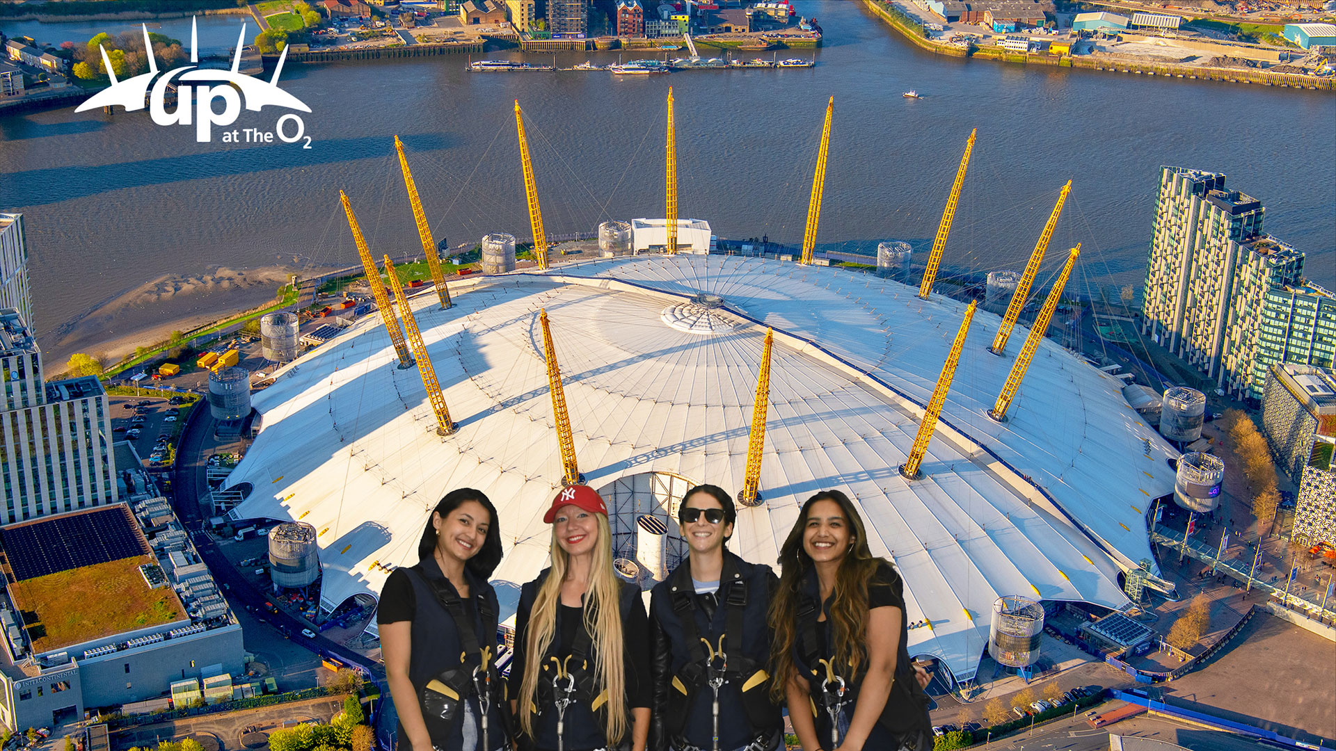 Up at the O2 is a fun and unique experience that everyone can enjoy. Image courtesy of Up at The O2 A group of women in front of an aerial view of The O2 Arena on a sunny day