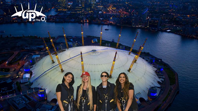 A group of women in front of an aerial view of the O2 Arena at night