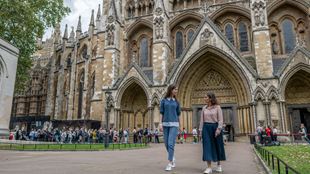 Two women are leaving Westminster Abbey standing in the background, with tourists queuing to enter this ioconic London landmark.