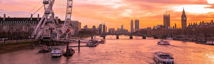 River Thames and London skyline at sunset with boats gliding along and Big Ben in the background.