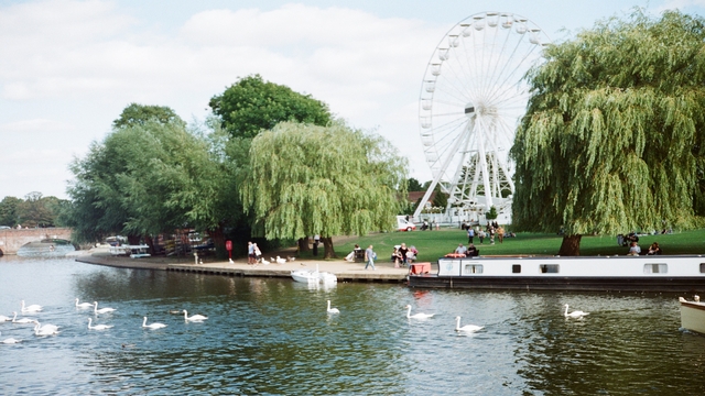 The river Avon in Stratford-upon-Avon. Image source: Unsplash/Young Shih A landscape photo of swans in the river and a ferris wheel in the background