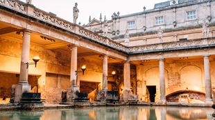 The roman baths pool lit up by orange torchlight.