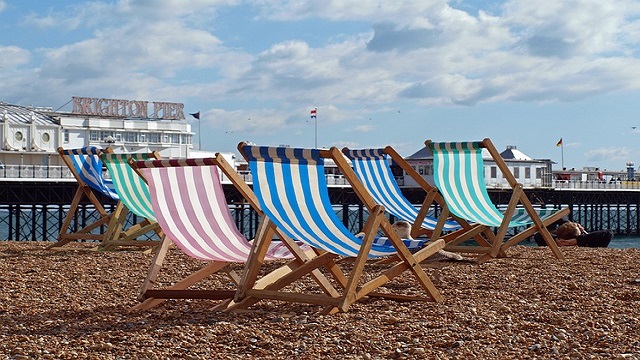 Pebbled beach next to Brighton Pier. © Pixabay/Willi Heidelbach Low angle shot of pink, blue and green deckchairs on a pebbled beach, with Brighton Pier in the background