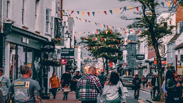 Shopping in North Laine, Brighton. © Unsplash/Evgeny Klimenchenko Two people holding hands, walking through a cobbled narrow highstreet with flag bunting zig-zagging across the street