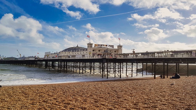 Landscape shot of Brighton Pier over the pebble beach and sea, with cloudy blue skies above