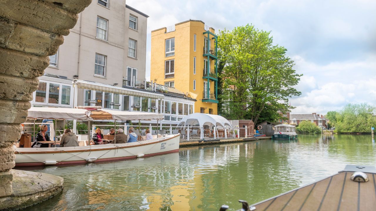 See the city of Oxford on a relaxing river cruise. Image courtesy of Golden Tours. Boats lined up against a white building on the river thames in oxford.