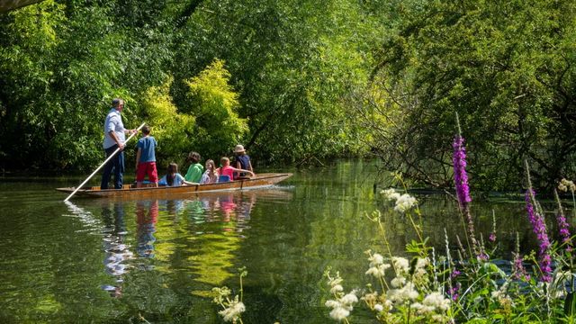 Go punting down the river Thames in Oxford. Photo by Noel Broda on Unsplash. A group of people go punting on a narrow boat down the river thames on a sunny day in Oxford.