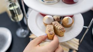 Someone picks one of the mini pastries presented on a plate part of the afternoon tea experience abord the London City Cruises excursion.