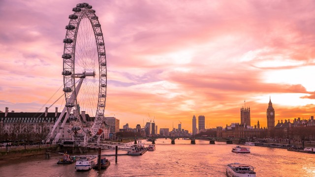 The London Eye, Big Ben and the Thames at sunset, with boats cruising down the river.