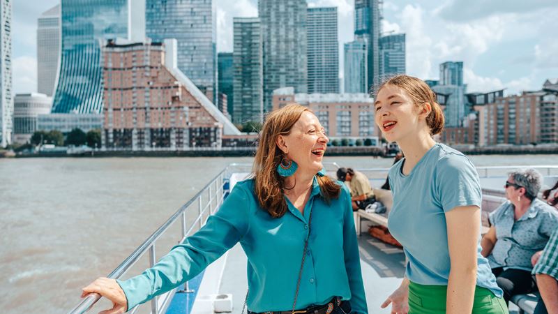 Two women are laughing standing on the top deck of one of City Cruises boats in London.