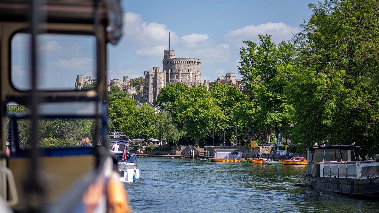 Take a 40 minute boat tour aboard the French Brothers Windsor riverboat and admire fantastic views on the royal town and Windsor Castle. © visitlondon.com/Michael Barrow View from the river on Windsor Castle surrounded by a green canopy.