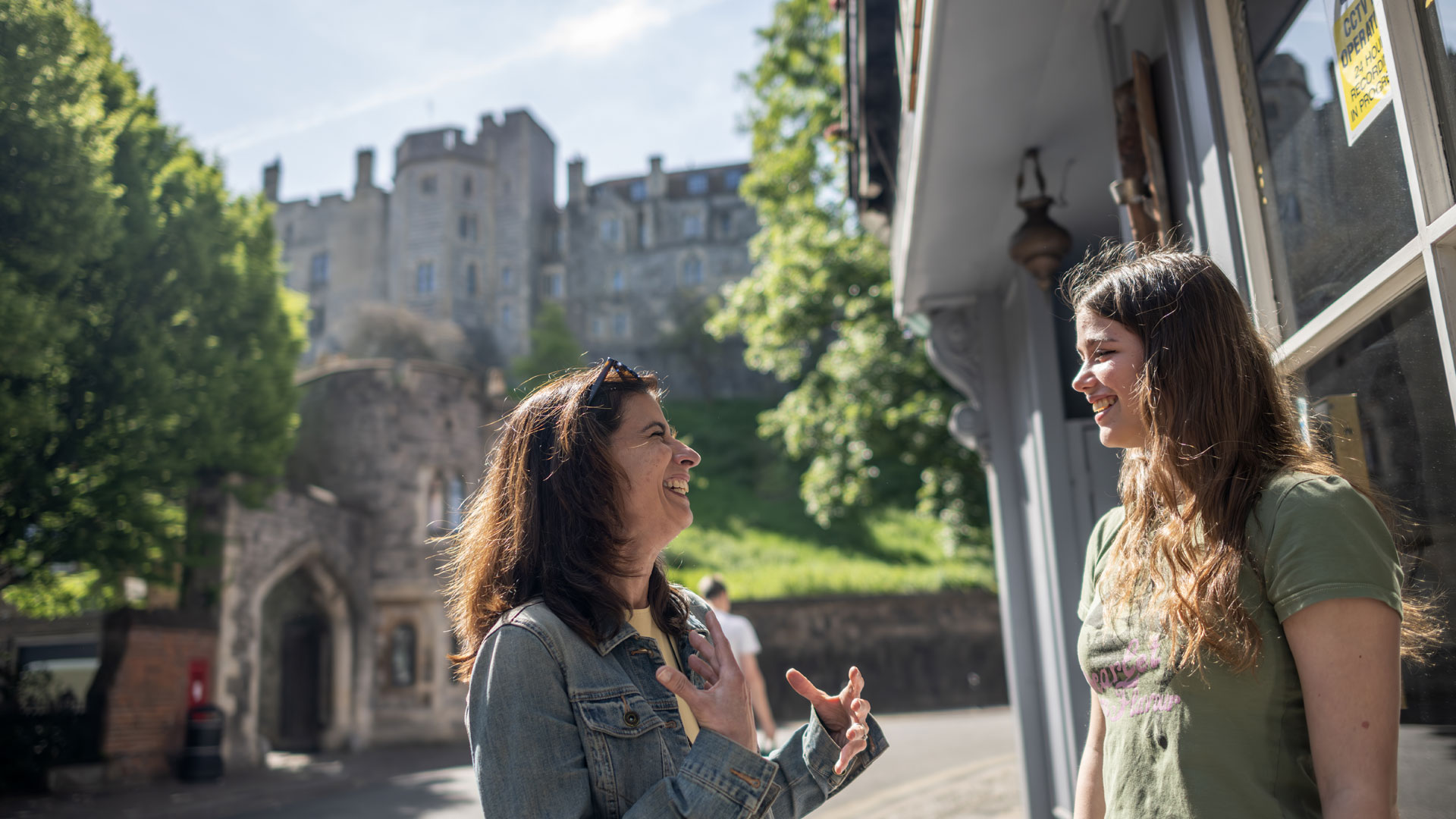 Hop aboard the doubledecker sightseeing bus and stop off at different locations across Windsor to visit attractions of your choice. © visitlondon.com/Michael Barrow. Two women discuss passionately while standing in the street with Windsor Castle shown in the backdrop.