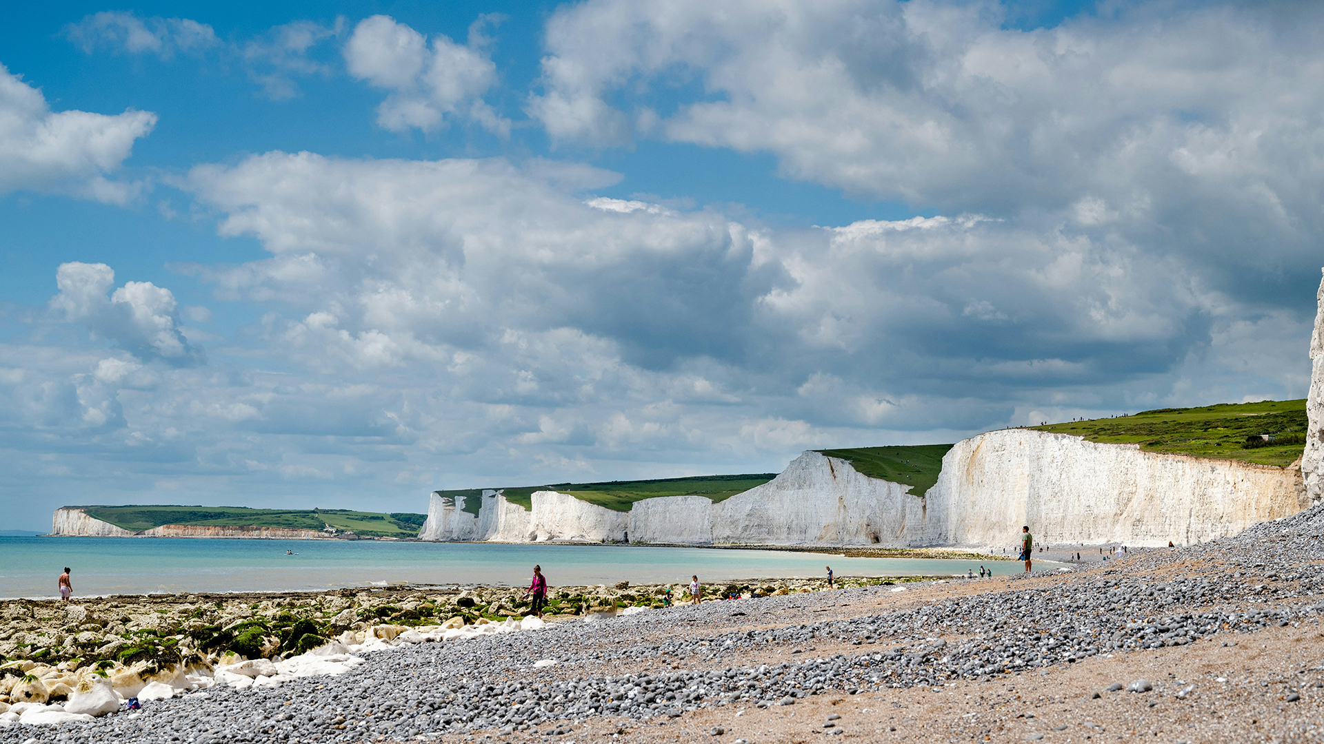 Birling Gap, East Sussex. Photo by Swati Kedia on Unsplash. The white chalk cliffs towering over the deserted pebbly beach of Birling Gap in East Sussex on a sunny day, with only a couple of people wandering about.