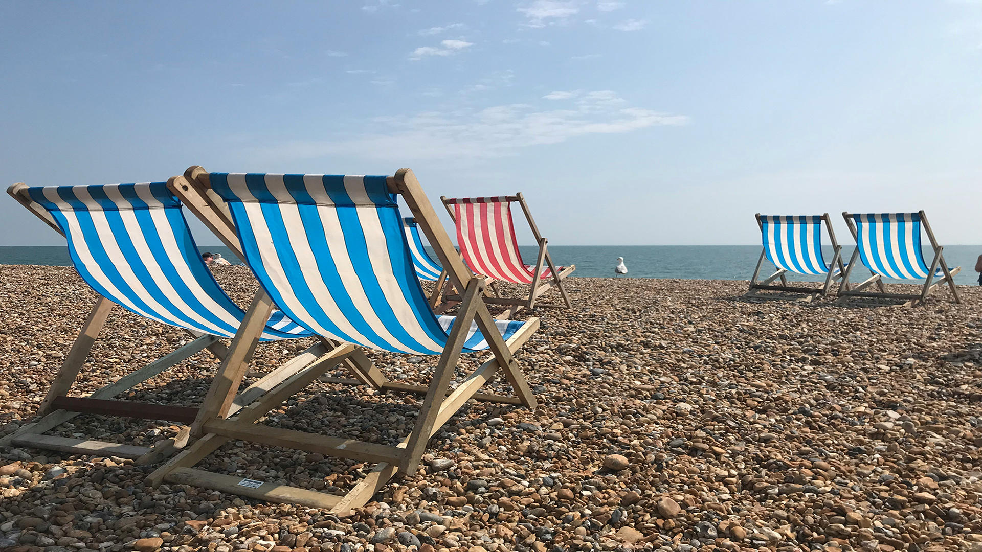 Brighton beach. Photo by Julia Hammond on Unsplash. Blue and white striped deck chairs on pebbly Brighton beach on a sunny day.