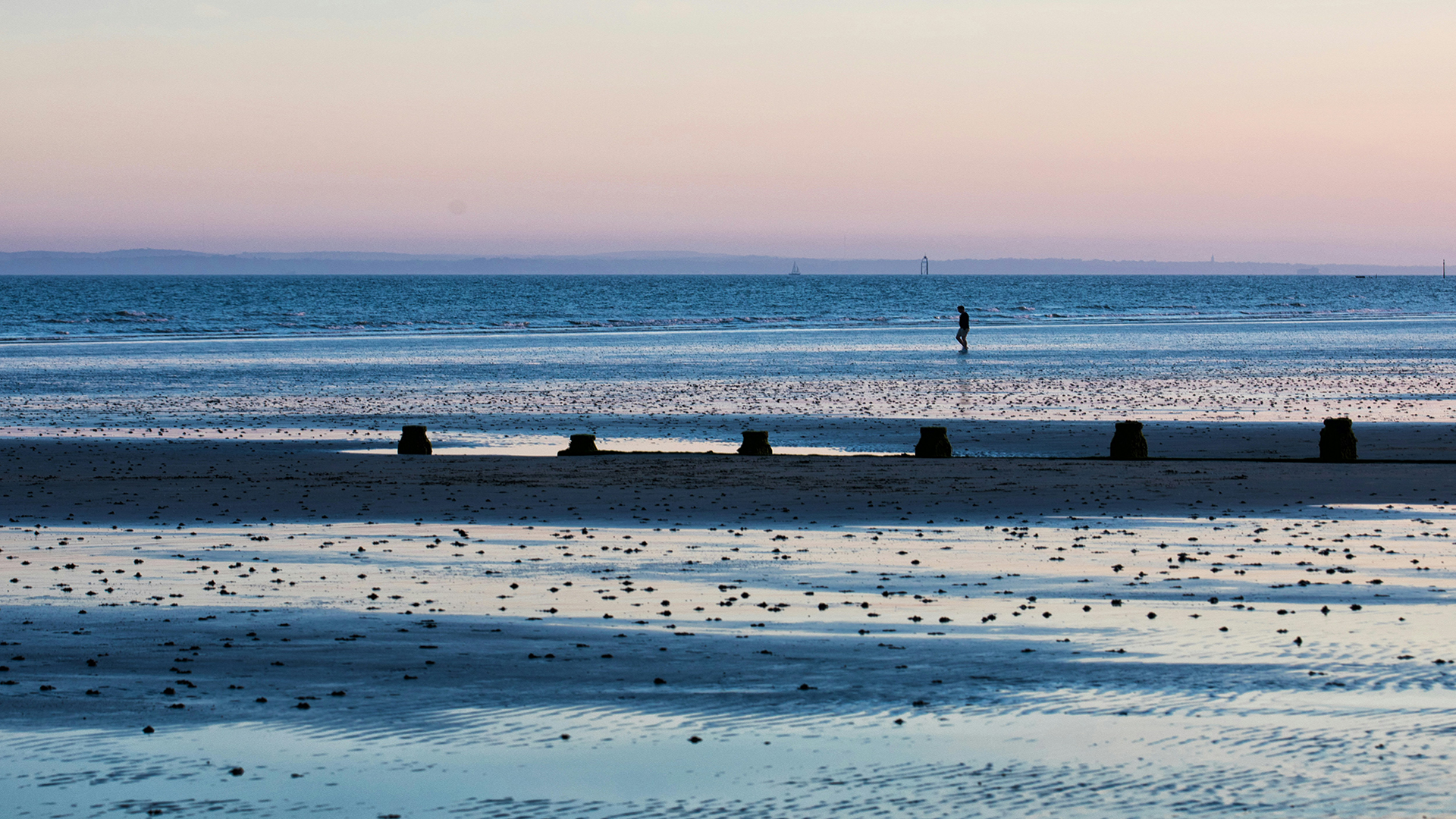 West Wittering, West Sussex. Photo by Rodney Minter-Brown on Unsplash. West Wittering beach in Chichester at sundown with a man walking in the distance.