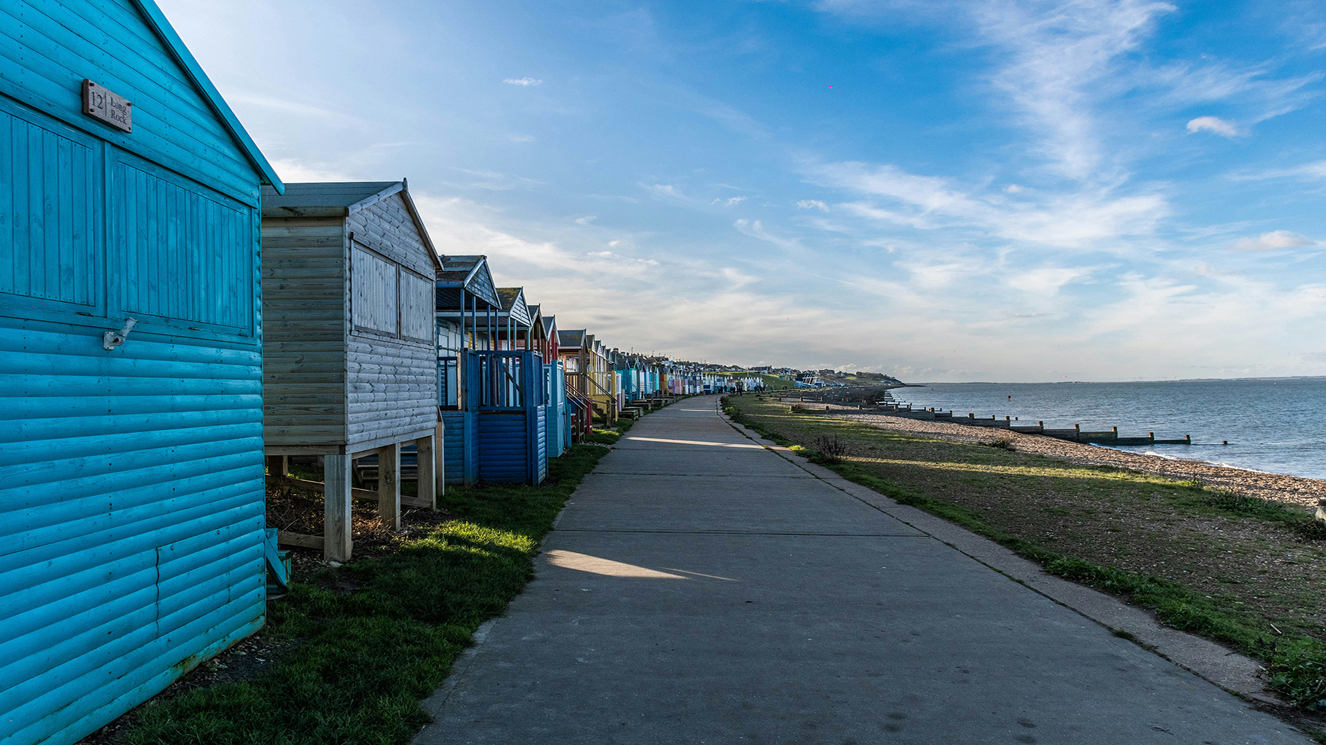 Whitstable, Kent. Photo by Arthur Knoepflin on Unsplash. Colourful beach huts lining the boardwalk by a shingle and pebble beach in Whitstable, Kent.